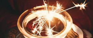 Sparkling lights flying out of a glass jar, against a night sky.