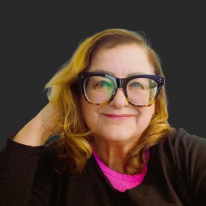 A smiling woman with fun glasses and a black & pink shirt. She is smiling, and leaning her head on her hand. She looks happy!