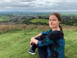 A woman sits on top of a hill and looks back at the camera, smiling slightly 