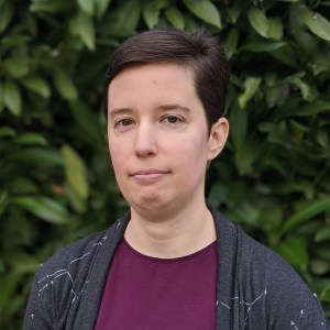 Jo Miles, a white nonbinary person with short brown hair, wearing a maroon shirt and gray cardigan with stars.