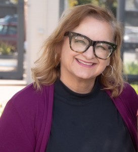 A smiling woman with shoulder-length auburn hair, wearing glasses.
